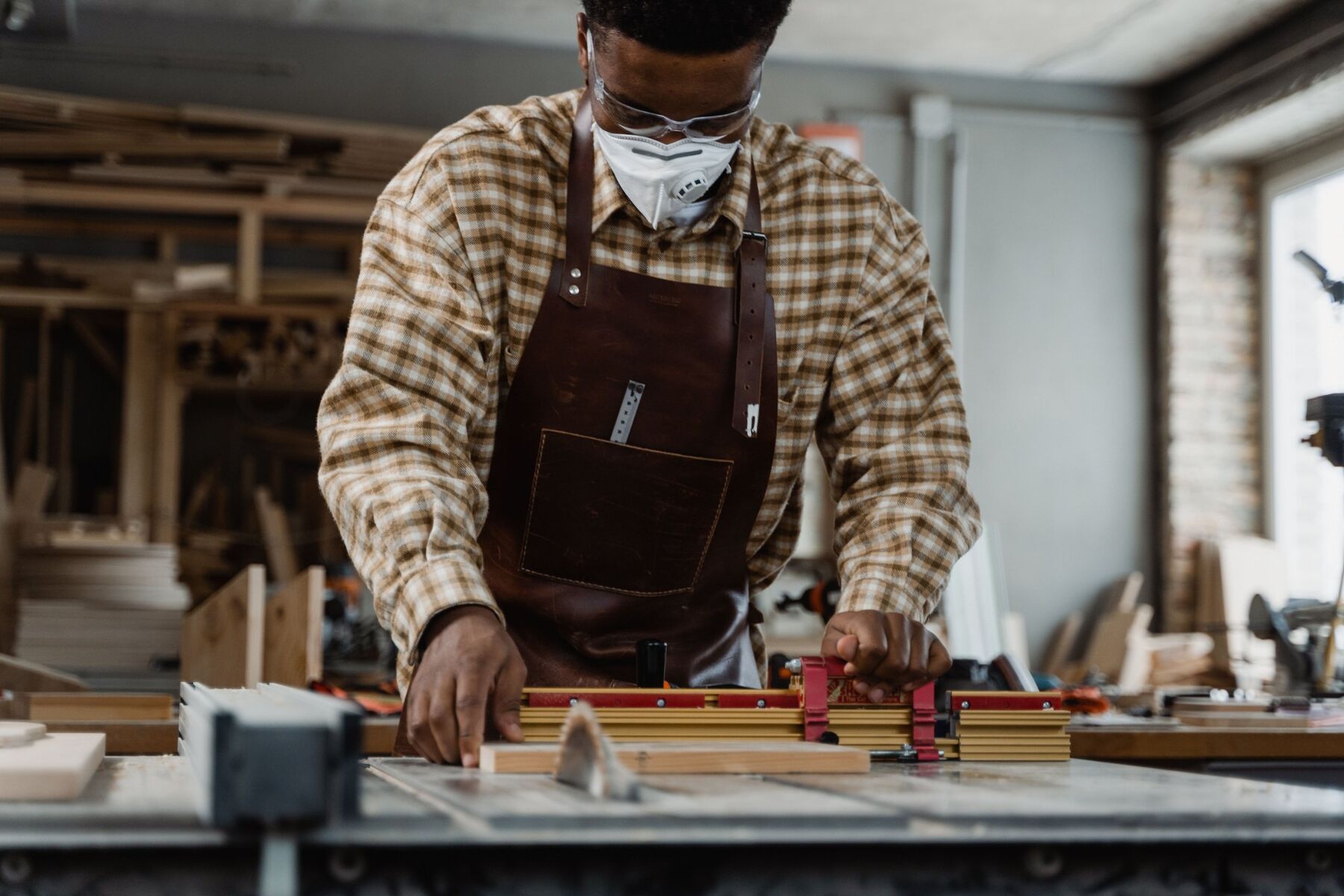 A carpenter cutting a timber board on a table saw in a busy workshop